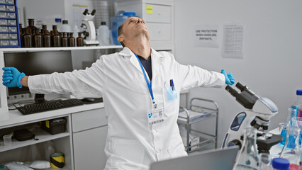 Handsome middle age man working diligently as scientist in his lab, stretching arms after hours at...