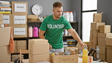 A focused young man in a volunteer shirt sorts donations in a cluttered warehouse.