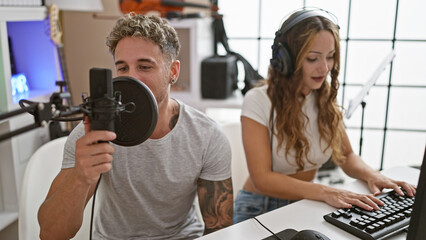 A man and woman record music together in a modern studio with professional equipment.