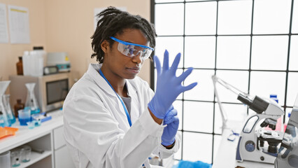 A young african american woman scientist wearing lab coat and safety glasses prepares for an...