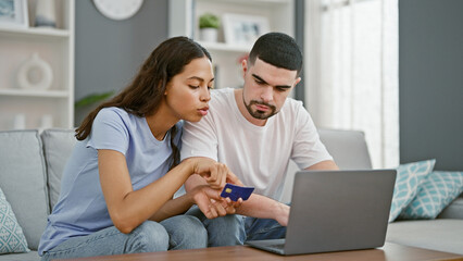 Beautiful couple in love, sitting together on sofa, engrossed in online shopping using a laptop and...