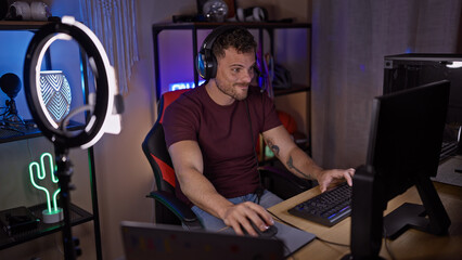 A focused young hispanic man with a beard uses a computer in a dimly lit gaming room at night.