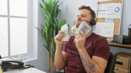 A content hispanic man in an office revels in money while wearing headphones.