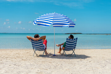 Two mans is sitting in chairs under parasol on a tropical beach. Summer vacation concept. © Paopano