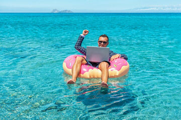 Businessman using laptop computer on an inflatable donut in the sea. Summer vacation concept.