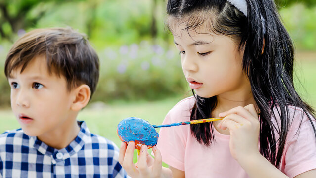 Happy group children in park, cute asian girl and boy with mix race friend, paint egg with blowing soap bubbles together on green grass in garden. Kids celebrate Easter holiday outdoor