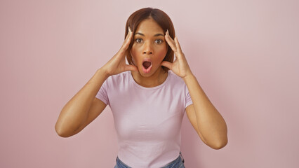 A surprised african american woman in casual clothing against a pink background expressing...