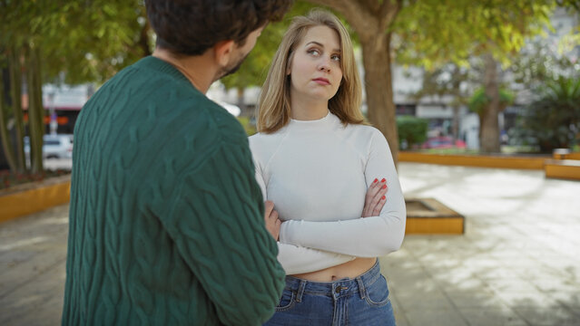 A couple encountering relationship tension in a city park, depicted by the man's concerned look and the woman's defensive posture.
