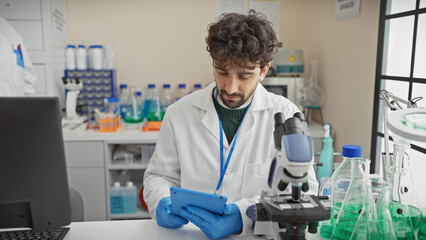 A focused man analyzing data on a tablet in a laboratory with scientific equipment and a microscope