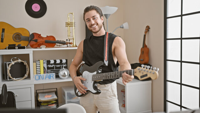 Young hispanic man musician smiling confident playing electrical guitar at music studio