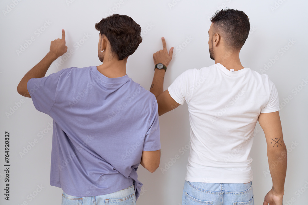 Sticker Homosexual gay couple standing over white background posing backwards pointing ahead with finger hand