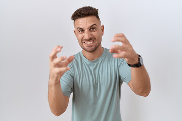 Hispanic man with beard standing over white background shouting frustrated with rage, hands trying to strangle, yelling mad