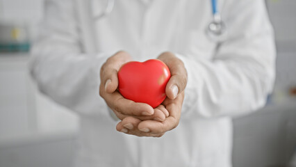 Healthcare professional man in lab coat holding red heart symbol in clinic for cardiology concept