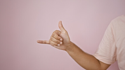 Young hispanic man makes a surfer hand gesture against a pink wall, isolated and expressive.