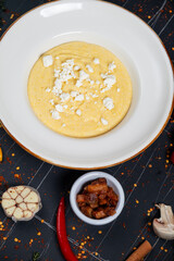 Banush or banosh is a Ukrainian dish prepared from cornmeal with cream topped with bacon, onion and bryndza closeup on the bowl on the wooden table. Vertical top view from above