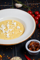 Banush or banosh is a Ukrainian dish prepared from cornmeal with cream topped with bacon, onion and bryndza closeup on the bowl on the wooden table. Vertical top view from above