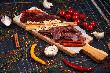 Top view of hands clanging glasses of beer together, near big wooden tray with delicious snacks, on wooden background