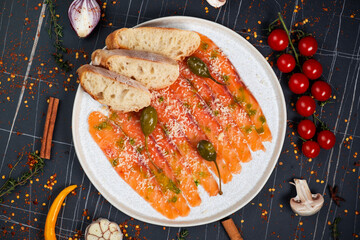 Salmon carpaccio with herbs, on a plate, on a dark background