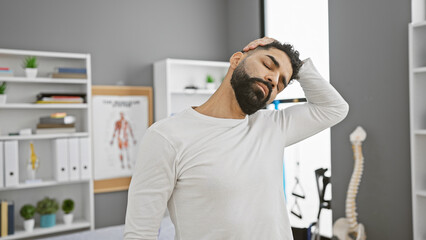 Fototapeta premium A young hispanic man with a beard in neck pain at a modern rehabilitation clinic.