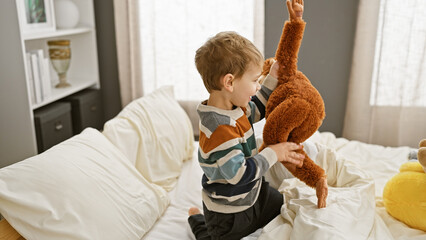 Blond boy playing with teddy bear on bed in a cozy bedroom setting, exemplifying innocent childhood.