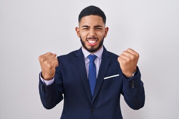 Young hispanic man wearing business suit and tie celebrating surprised and amazed for success with arms raised and eyes closed. winner concept.