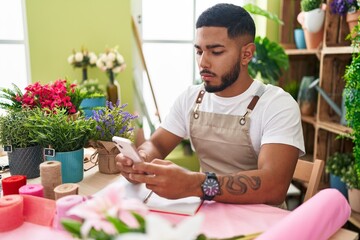 Young latin man florist using smartphone at flower shop - obrazy, fototapety, plakaty