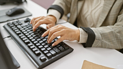 Mature woman typing on a keyboard in an office setting, reflecting everyday professional life. - obrazy, fototapety, plakaty