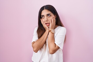 Young arab woman standing over pink background tired hands covering face, depression and sadness,...