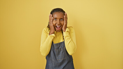 A surprised african woman with hands on her head against a yellow background expressing emotion.