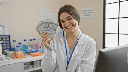 A smiling young woman in a lab coat holds peruvian currency in a clinical laboratory setting.