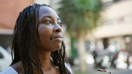 Thoughtful african american woman with curly hair gazes outdoor in city environment.