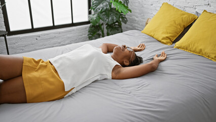 Relaxed woman lying on a bed indoors with yellow accents and green plants.