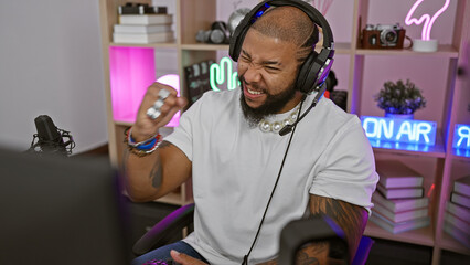 African american man streaming in a vibrant gaming room with neon lights, laughing with headphones...