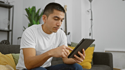 Hispanic man using tablet in a modern living room, portraying technology use in home lifestyle.