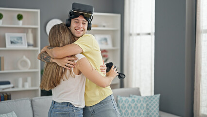 Beautiful couple wearing virtual reality glasses hugging each other at home