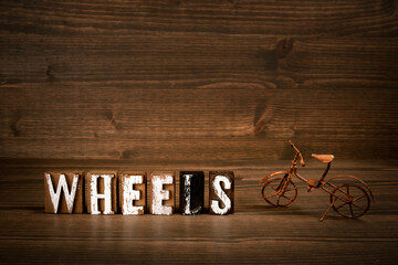 WHEELS. Text from alphabet blocks and rusty miniature bicycle on wood texture background