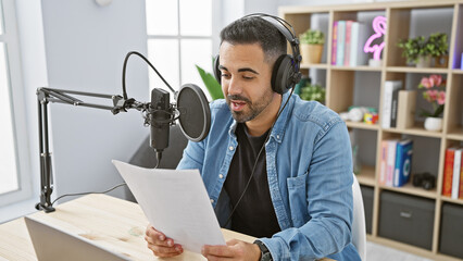 Handsome hispanic man with beard reading script in radio studio