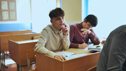 Schoolboys at a desk during class. The boy eats an apple.