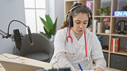 Hispanic woman in lab coat with stethoscope hosting a podcast in a modern studio room
