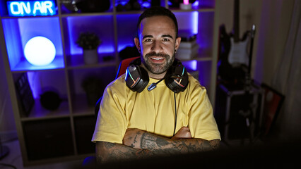 A bearded, handsome hispanic man wearing headphones poses in a room with neon lighting, embodying a casual and modern indoor atmosphere. © Krakenimages.com