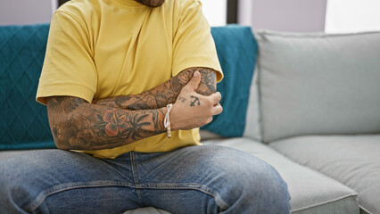 A tattooed young man in a yellow shirt holding his elbow in pain indoors