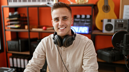 Smiling young man with headphones in a music studio surrounded by instruments and recording...