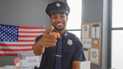 A smiling policeman pointing at the camera in a voting center with an american flag in the...