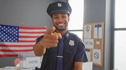 Foto auf Leinwand A smiling policeman pointing at the camera in a voting center with an american flag in the background. © Krakenimages.com
