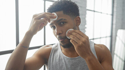 African american man grooming using cotton pads in a well-lit living room.