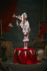 Siamese twin girls in white vintage costumes with makeup standing over dark retro circus backstage background. Creative spooky play. Concept of circus, theater, performance, show, retro and vintage - obrazy, fototapety, plakaty