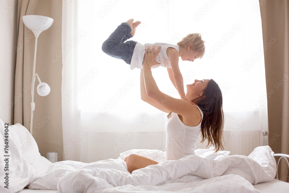 Poster Beautiful blond child and his mother, playing at home in the morning in bed, smiling, laughing and having fun