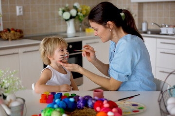 Mother painting on little blond toddler boys' face easter bunny