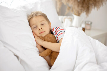 Obraz na płótnie Canvas Sweet blond preschool child with teddy bear, lying in bed sick,