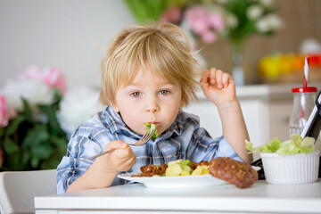 Little toddler child, blond boy, eating boiled vegetables, broccoli, potatoes and carrots with fried chicken meat at home